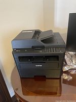 Front and side view of Brother MFC-L2750DW multi-function laser printer on table.