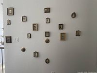 Full wall view showing 15 small framed pictures hanging on a white wall in various frame shapes and styles including round, oval, and rectangular.