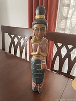 Photo showing a wooden statue of a praying lady with detailed features and colorful clothing, standing on a wooden table.
