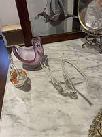 Three glass swans displayed on marble surface in front of a mirror, including a purple swan, clear swan, and a small clear swan with orange accents
