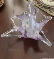 Oblique top-down view of irregular shaped glass vase showing purple tint and multiple pointed tips extending outward, displayed on wooden table.