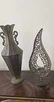 Photo showing two metal decorative items: a 20-inch vase with handles and an openwork metal sculpture.