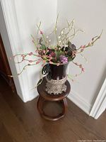 Vase with artificial flowers placed on a small wooden stool beside a white wall