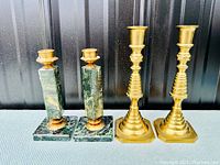 Two pairs of candlesticks displayed side by side: a green marble pair with brass holders and a brass pair with tiered bases.