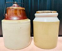 Two stoneware crocks, one with brown glazed top and metal handle, the other beige with wooden lid, shown side by side.