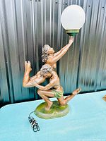 Full view of lamp showing nude couple sculpture holding frosted globe light on a decorative base with electric cord.