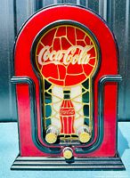 Front view of the Coca-Cola AM FM radio showing the stained glass style front panel with Coca-Cola logo and bottle motif, and three gold-colored knobs.