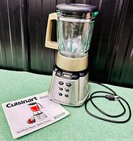 Front view of the full blender assembled with manual beside it on green surface.