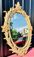 Front view of the large oval wall mirror showing detailed floral carvings and clear reflective glass.