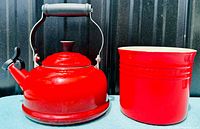 Red Le Creuset kettle next to red stoneware utensil crock on blue surface with metal backdrop