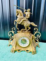 Front view of complete brass clock on green surface with metal siding background