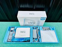Wii original box and packaging with accessories including cables, manuals, and sensor bar.