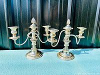 Photo showing the matching pair of silver plated candelabra with three candle holders and decorative flame finials.