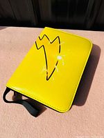 Photo of the yellow zippered Pokemon card album with Pikachu tail silhouette on front