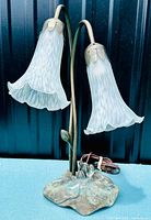 Front view of the lamp showing two tulip shaped white frosted glass shades with metal leaf fittings and patina lily pad base.