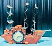 Full view of United Clock Corp wooden clipper ship mantel clock with metal spiral sails. Clock shaped as ship with nautical fish metal accents and ship wheel design clock face.