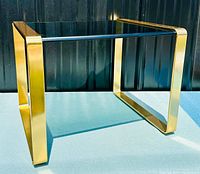Side angle front view showing rectangular polished brass frame and smoked glass top surface of the end table.