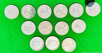 14 Canadian silver quarters arranged on green felt surface, showing projectile animal designs and wear from circulation.