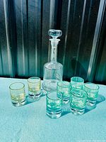 Clear glass decanter with stopper and seven controlled bubble glasses arranged around it on a blue surface against a dark background.