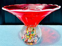 Front view of the red Murano glass center bowl with paperweight base, showing flared rim and colorful inclusions in the clear glass base.