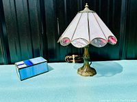 Photo showing both the vintage stained glass table lamp with brass base and the blue stained glass trinket box closed on a turquoise surface.