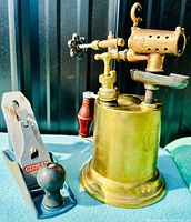 Stanley wood plane and brass blowtorch side by side on blue cloth showing both items in great condition.
