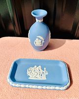 Blue Wedgwood jasperware vase and tray with white classical reliefs, placed on soft pink surface.