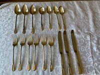 Full view of spoons, forks and knives laid out on a patterned white cloth, showing the floral design on handles.