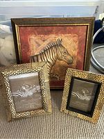 Three zebra print animal art frames arranged on carpet, showing the large painted zebra frame behind two smaller photo frames with animal print borders.
