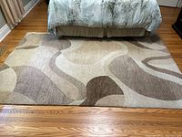 Photo of rectangular area rug in beige and brown abstract pattern on hardwood floor under bed