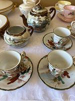 Front angle view of teapot, sugar bowl, and 3 tea cups with matching saucers on tablecloth