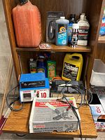 Full view of auto supplies on wooden shelves and table including gas can, fluid containers, battery charger, power supply unit, and hitch kit box.
