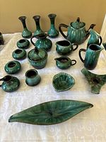 Full view of all Blue Mountain pottery pieces arranged on white patterned fabric showing vases, teapot, pitchers, sugar bowl, and other items