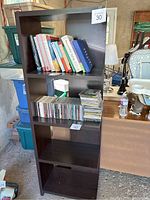 Front angled view of the bookshelf showing all four shelves, some with books and CDs for scale, located in a garage space.