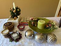 Full lot showing candles, holders, decorative bowl with balls and floral accents on tabletop.
