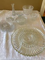 Overall view of all crystal pieces including candy dish, bud vase, plates, serving tray, and candle holders on white tablecloth.