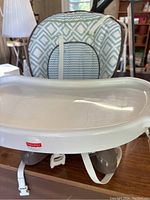 Front view of Fisher-Price booster seat showing padded fabric back and white plastic tray with Fisher-Price logo