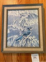 Full view of framed print depicting a blue jay perched on pine branches with frost or snow, wooden frame with beige matting.