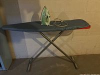 Ironing board with grey cover and Philips iron placed on top against a wall