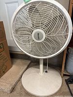 Front view of white Lasko floor fan showing circular grille and dusty fan blades on round base.
