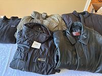 Front view of four men's outerwear items laid on a bed, including fleece, quilted jacket, leather jacket and puffer vest.