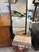 Mirror leaning against a surface with decorative book and floral magazine holder in front.