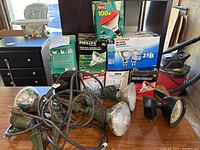 Photo showing four metal outdoor flood lights with cords and several boxes of replacement halogen bulbs from brands like Sylvania and Philips.