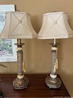Two matching accent lamps with fabric shades placed on a wooden surface against beige wall.