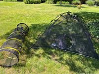 Wide shot showing the mesh pop-up pet tent next to the mesh tunnel on grass.