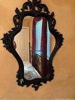 Front view of the vintage black ornate mirror showing full shape and intricate floral and scroll resin details in the frame