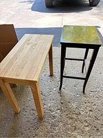 Pair of small wooden tables side by side on outdoor floor, showing different styles and finishes.