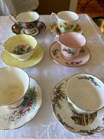 Top view of six bone china teacups and saucers in various floral and landscape designs, all with gold trim.