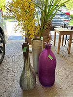 Photo of three large decorative vases with artificial greenery placed on ground in garage area, showing each vase's color, shape, and contents.