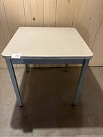 Front view of vintage table showing white square laminate top with gray metal legs.